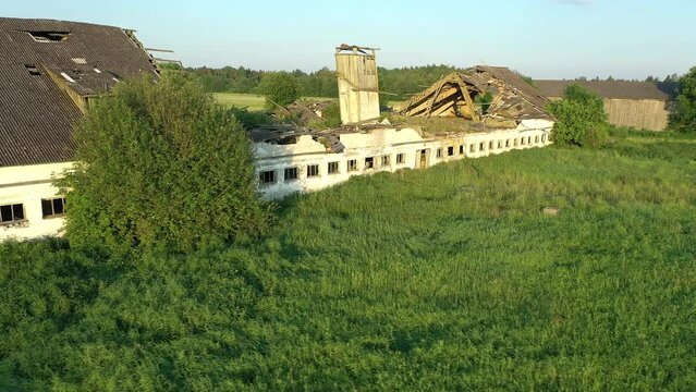 Koeru.Estonia-July 5.2021: Drone shot of a ruined soviet farm building showing the decaying structure slowly getting taken over by nature. Camera moving sideways and turning left.
