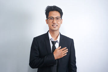 Young Asian man wearing suit smiling while holding hands on his chest