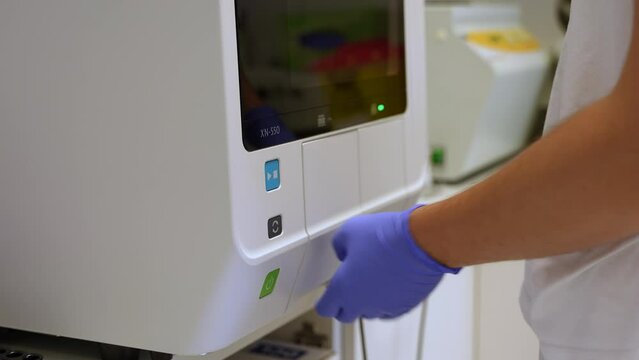 A laboratory technician loading a blood sample into an analyser (hematology machine) for medical analysis