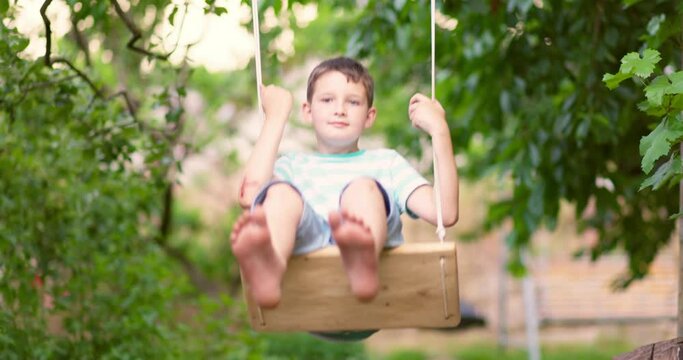Happy little boy swinging on a swing in the garden. 