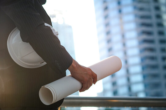 An engineer holds a building plan and is working and supervising the construction, he is reading plans for production, business and investment.