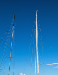 Sailboat Masts Against Blue Sky with a Daytime Moon Setting.