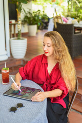 Beautiful blonde woman artist and illustrator made an idea about a concept of her drawing, sitting by the table with electronical tablet and stylus