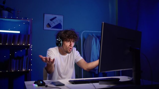 Young arabic man plays computer games at home with neon light. The streamer is angry during the broadcast. Male online player is upset about the defeat.