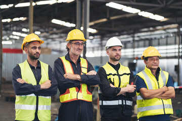 Group of male factory workers standing together with crossed arms and smiling in industry factory, wearing safety uniform and helmet. Factory workers working in factory