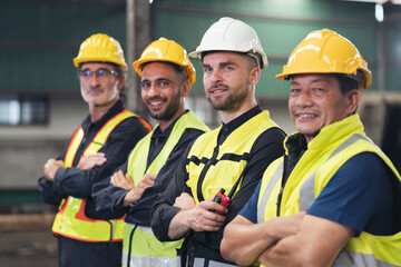 Group of male factory workers standing together with crossed arms and smiling in industry factory, wearing safety uniform and helmet. Factory workers working in factory