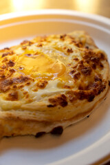 Traditional Georgian cuisine. Ajara khachapuri on paper plate. Filled with cheese and topped with raw egg and butter, cheese-filled bread. Delicious food