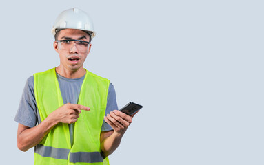 Amazed engineer using cell phone. Impressed engineer pointing finger at mobile phone. Young engineer holding cell phone on isolated background