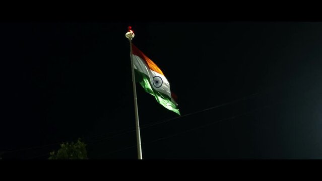 Indian tri colour national flag hoisted on a tall poll in front of a indian railwaystation at night.