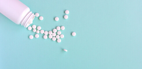 水色の背景に散らばる複数の白い錠剤と薬のボトル - obrazy, fototapety, plakaty