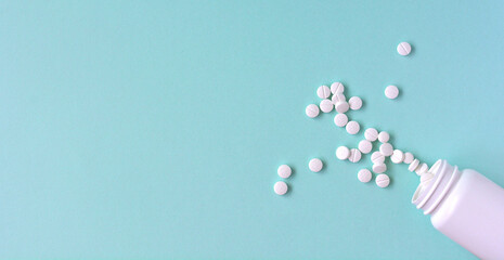 水色の背景に散らばる複数の白い錠剤と薬のボトル - obrazy, fototapety, plakaty