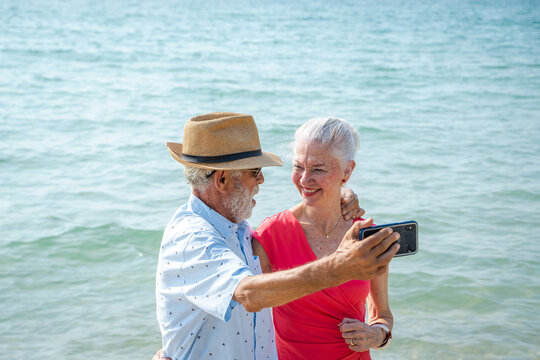 Mature couple taking pictures together by the sea during summer seaside trip,Happy retirement,Ocean and outdoor embrace with love.