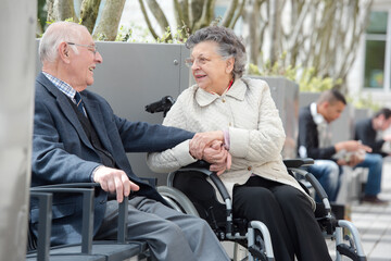 Fototapeta na wymiar senior man with woman in wheelchair sat outside