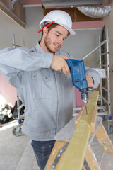 carpenter drills a hole with an electrical drill on wood