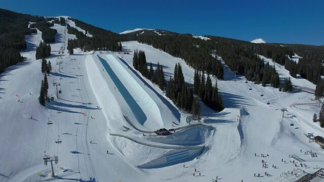 Drone aerial Copper Mountain winter ski snowboard resort half pipe training practice tricks competition Colorado early morning sunlight fresh snow ski lift crowd cinematic pan to the right motion 4k