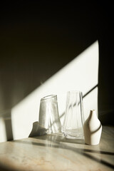 A room with various objects such as warm sunlight, shadows of grass leaves, a vase on a table, and cups