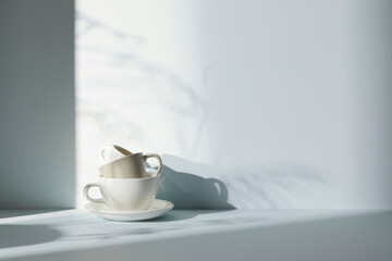 A room with various objects such as warm sunlight, shadows of grass leaves, a vase on a table, and cups