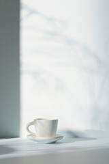 A room with various objects such as warm sunlight, shadows of grass leaves, a vase on a table, and cups