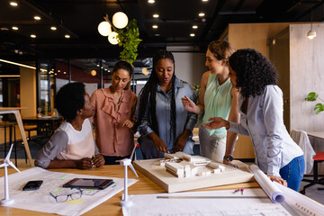 Diverse female architects in discussion using model and blueprints in casual office meeting