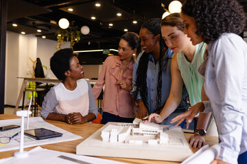 Diverse female architects in discussion using model and blueprints in casual office meeting