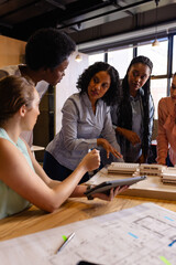 Diverse female architects in discussion using model, blueprints and tablet in casual office meeting