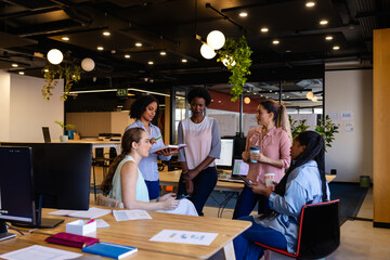 Diverse female colleagues in discussion using tablet in casual office meeting