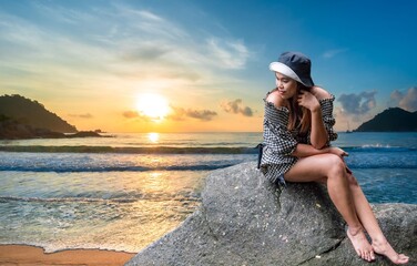 tourist sitting on a rock watching the sunset sea nature.Surfer woman wearing a hat, fashion dress, traveling, sitting on a stone, natural scenery, relaxation