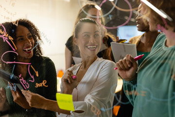 Diverse creative female colleagues in discussion brainstorming making notes on glass wall in office