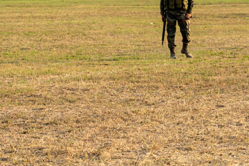 Security guard with rifle AK-47 standing on field to protect the area.