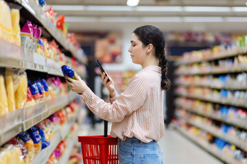 Side view of caucasian woman scan qr code of product using smartphone. Shelves with food in...