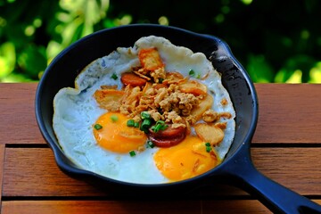 Indochina pan-fried eggs is fried egg topping with bacon and chinese sausage in hot pan.
