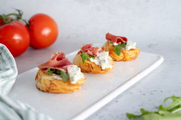 On the kitchen table is a board with fresh bruschetta with ham and cheese. Along with tomatoes and greens