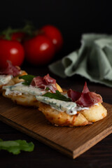 On the kitchen table is a board with fresh bruschetta with ham and cheese. Along with tomatoes and greens