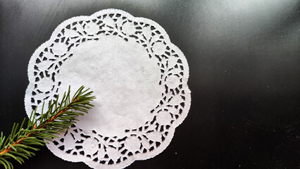 Black frame, white round napkin, green pine branch on background with reflections and sparkle of light. Abstract location for photo shoot. Christmas. Concept of caring for nature ecology