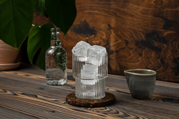 Espresso tonic cold refreshing coffee drink in the making. A glass filled with ice cubes, bottle of tonic water and espresso on wooden background