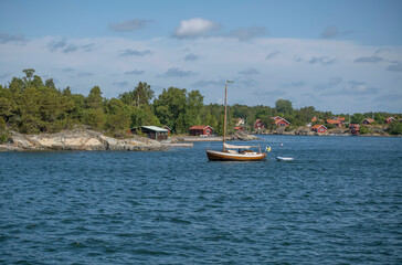 Fototapeta na wymiar Island, skerries and islet, in the middle part of the archipelago, summer houses, an old sailing boat passing on the bay at the island Möja, a sunny summer day in Stockholm