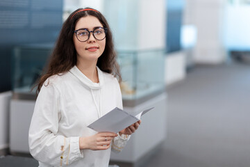 Portrait of pretty young caucasian girl student wearing eyeglasses visiting museum exhibition. Light hall in background. Concept of cultural education and Museum's Day