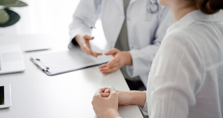 Doctor and patient discussing current health examination while sitting at the desk in clinic office. The focus is on female patient's hands, close up. Perfect medical service and medicine concept