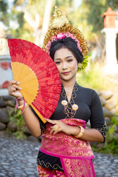 Beautiful bali asian portrait women with crown and red fan  in traditional costumes in bali garden, indonesia
