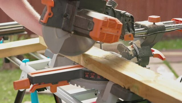 Slow motion shot of a carpenter using a saw to cut through decking boards with dust rising