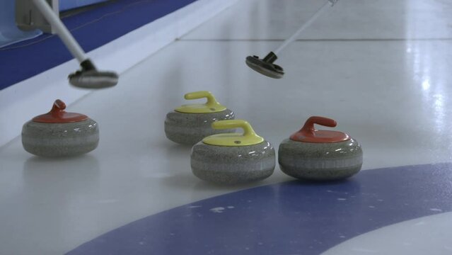 Curling stone collide with other curling stones. Players sweeping.