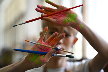 Artist hands soiled with watercolor paints holding brushes and smiling to camera. Art, hobby and leisure activity concept