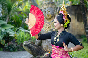 Woman poses in front of a Buddha statue in a traditionally costume and a crown in hair