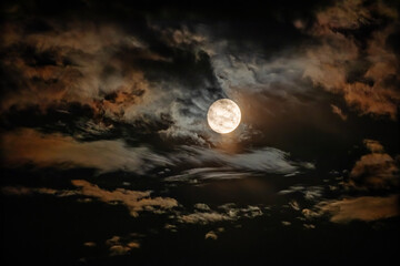 The full moon is surrounded by dramatic colored clouds in the dark night sky. HDR photo taken through a telephoto lens