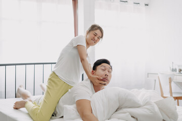 Fototapeta premium Funny asian couple wife giving husband hurt massage in white bedroom.