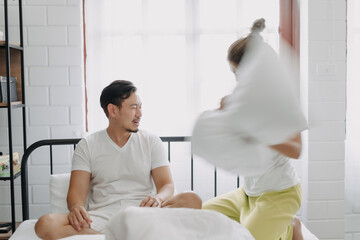 Asian wife and husband playing pillow fight funny and laugh on the bed.