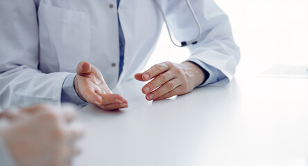 Doctor and patient discussing current health questions while sitting at the table in clinic office, only hands closeup. Medicine concept