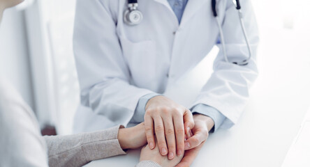 Doctor and patient sitting at the table in clinic office. The focus is on female physician's hands reassuring woman, only hands close up. Medicine concept