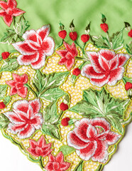 Green kebaya cloth with intricate embroidery of red flowers.