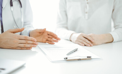Doctor and patient discussing current health questions while sitting near of each other at the table in clinic, just hands closeup. Medicine concept